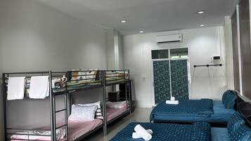 A dormitory-style room with bunk beds, a small seating area, and a door leading to a bathroom.