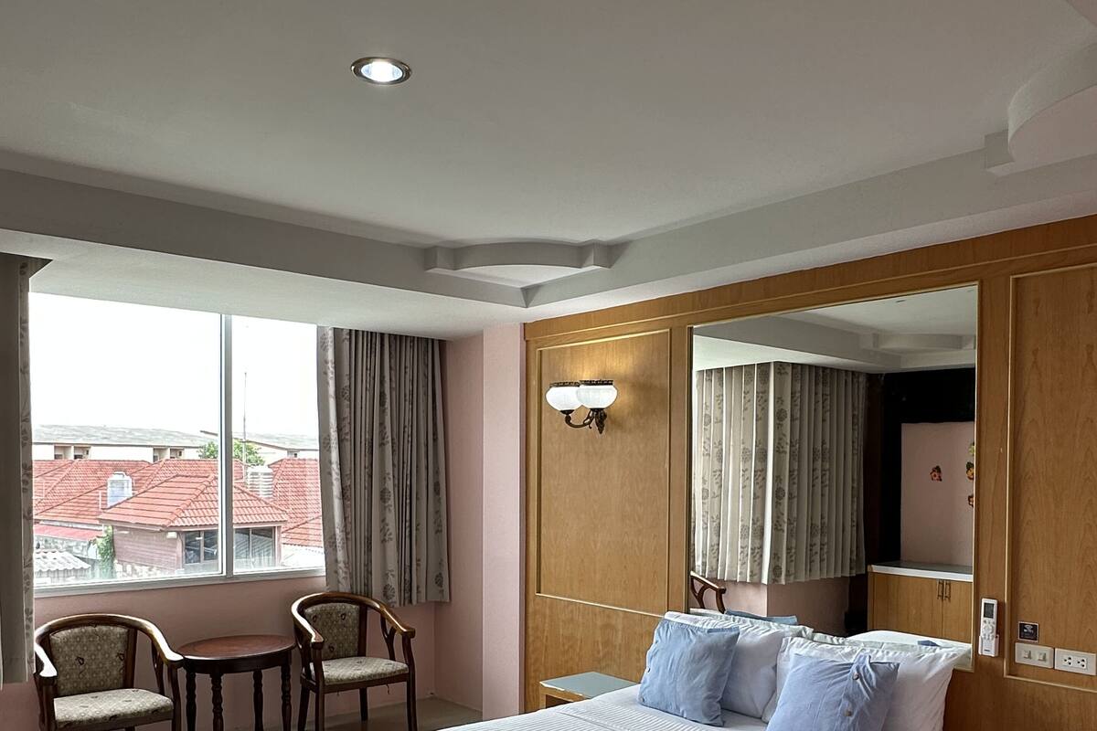 A hotel room with a large bed, two chairs, a small table, a mirror, and a window with curtains.