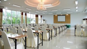 Une salle de conférence avec des rangées de tables et de chaises, un grand écran et un lustre.