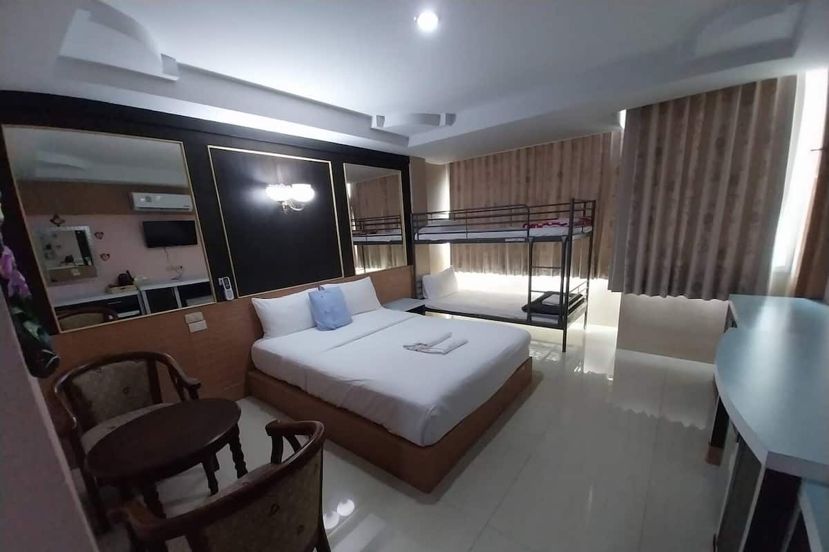 A hotel room with a bed, a desk, a chair, a bunk bed, a mirror, and a television.