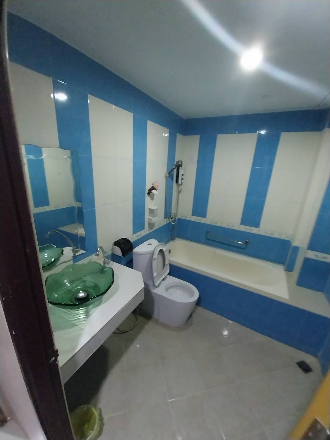 A bathroom with a white toilet, a green glass sink, and a bathtub.