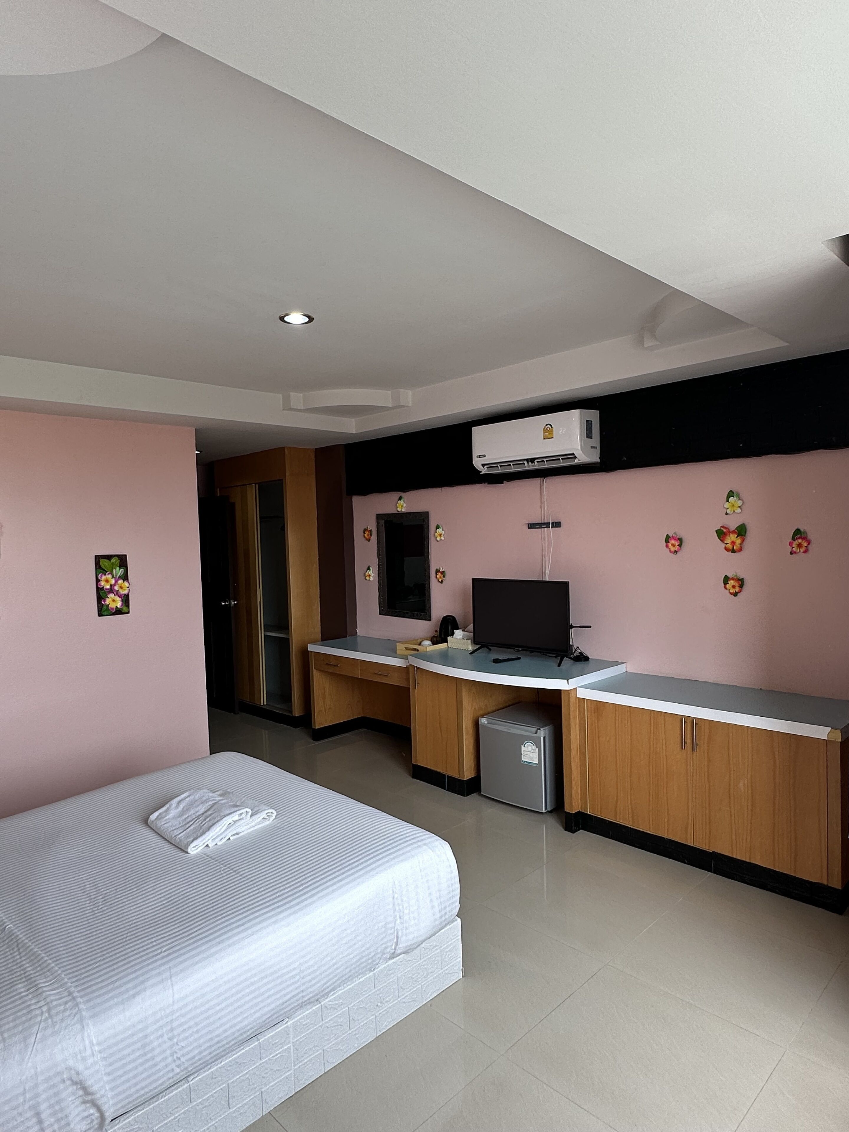 Une chambre d’hôtel de taille réduite, équipée d’un lit, d’un bureau, d’un petit réfrigérateur et d’un appareil de climatisation.