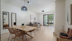 Un amplio comedor con una mesa de madera y sillas de mimbre, un conjunto de sofás, y un ventanal con vistas al exterior.