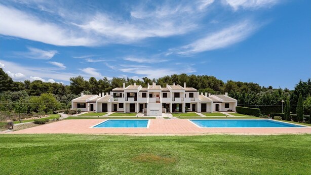 Una villa moderna con piscina, rodeada de un césped cuidado y árboles.