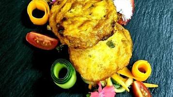 A dish with a golden-brown crust, surrounded by colorful garnishes and a dark textured background.