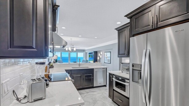 A modern kitchen with stainless steel appliances, dark cabinetry, and a large island with a sink. - Beach View 1 Bedroom 902 (Sarasota)