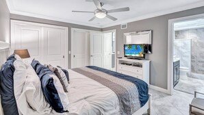 A bedroom with a bed, a ceiling fan, a TV, and a bathroom with a shower and toilet. - Beach View 1 Bedroom 902 (Sarasota)