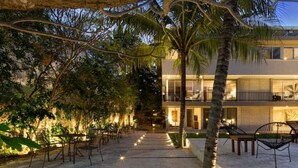 A modern two-story building with a balcony, surrounded by palm trees and outdoor seating. - Caseiba Peaceful Stays 5 (Merida Yucatan,)