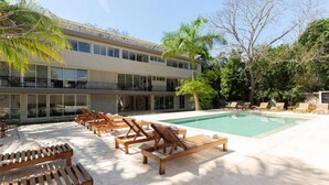 Ein Poolbereich mit Liegestühlen und einem Pool, umgeben von einem Gebäude mit großen Fenstern und einem Balkon.