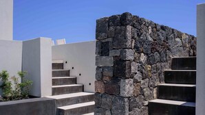 A modern outdoor staircase with a stone wall on one side and a flat, white-tiled area on the other. - RyoLithos Suites (Santorini)