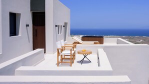A modern white building with a wooden door, a small window, and a balcony with a table and chairs. - RyoLithos Suites (Santorini)