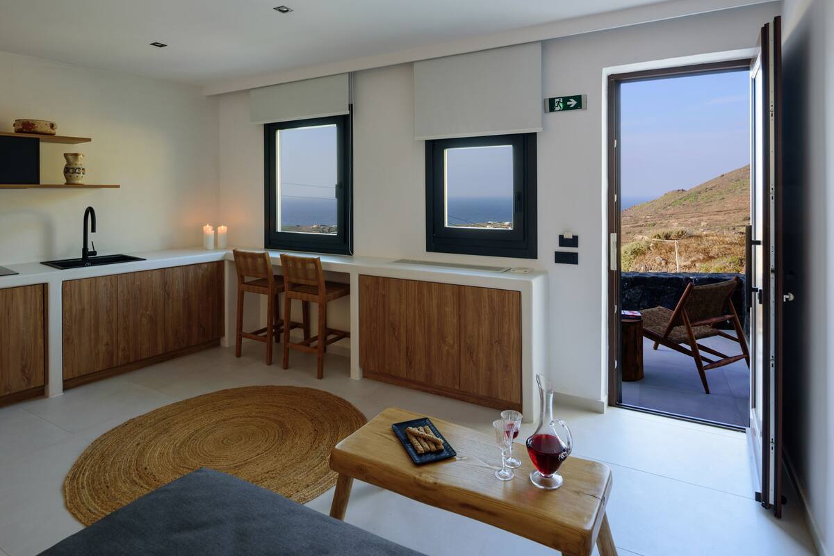 Una cocina moderna con comedor, vistas al mar y una zona de estar acogedora con alfombra y una mesa con un libro y vasos.