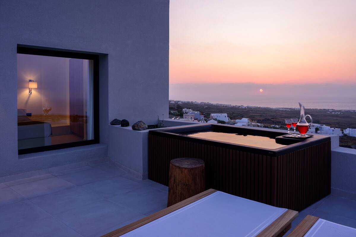 Una terraza moderna en la azotea con vistas a la puesta de sol sobre el mar, una zona de bar y un área de estar con una lámpara.