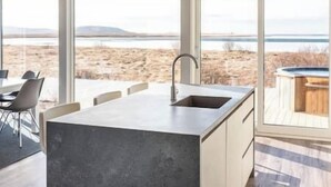 A modern kitchen with a large island, a sink, and a view of the beach.