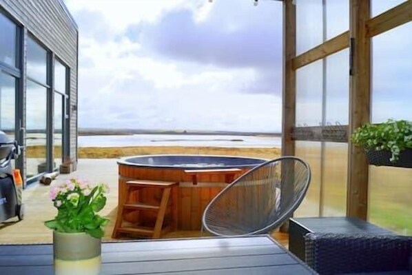 A patio area with a hot tub, outdoor seating, and a view of the beach. - ---Lakefront Villa--- (Laugarvatn)