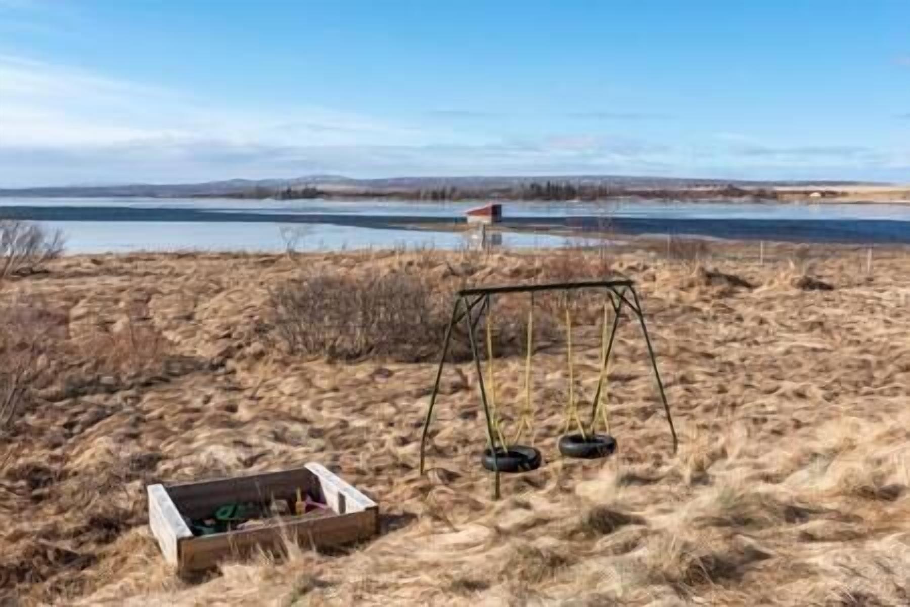 A swing set in a grassy area with a lake and distant hills.