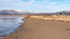 A beach with a small building, a clear sky, and snow-capped mountains in the background.