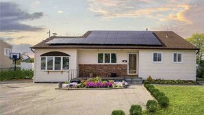 Una casa de una sola planta con paneles solares en el techo, un porche delantero y un pequeño jardín.
