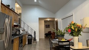 Una cocina pequeña con refrigerador, estufa y gabinetes. Hay una mesa de comedor con sillas y una planta en maceta.