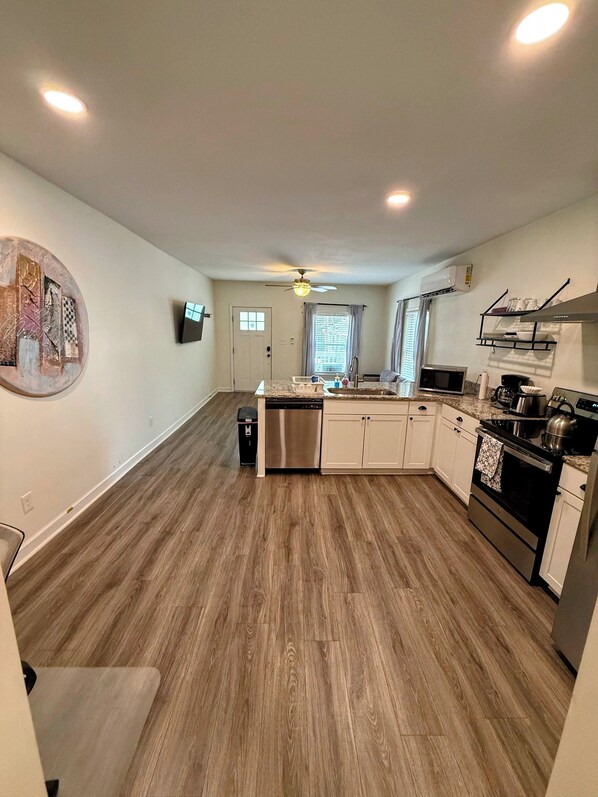 A modern kitchen with wooden flooring, a dishwasher, a stove, and a ceiling fan.