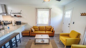 Een woonkamer met een bank, fauteuils, een salontafel en een keuken met apparatuur.