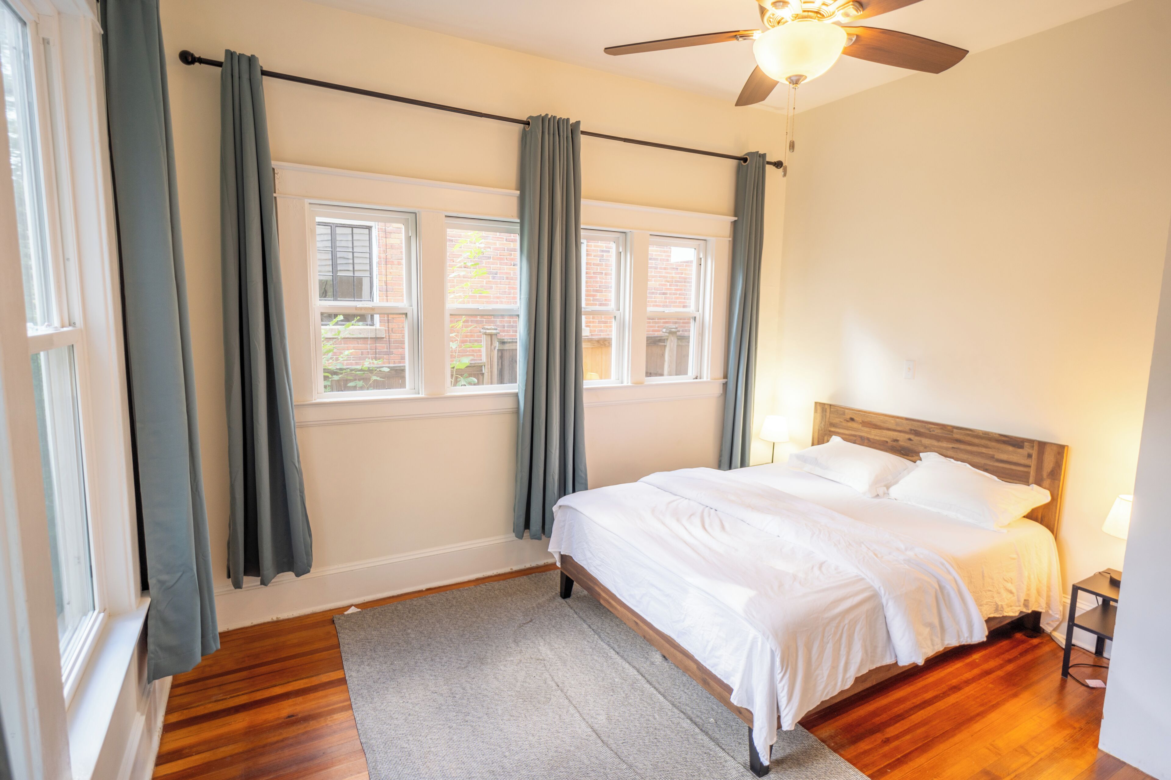 Un dormitorio con cama, ventilador de techo, ventana con cortinas y vistas al exterior.