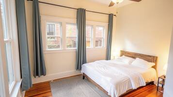 Un dormitorio con cama, ventilador de techo, ventana con cortinas y vistas al exterior.