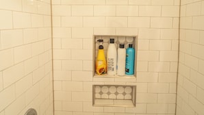 A shower with a handheld showerhead, a shelf with toiletries, and a tiled wall. - Walk to Duke Campus!  3 Bedroom in Trinity Park! (Durham)