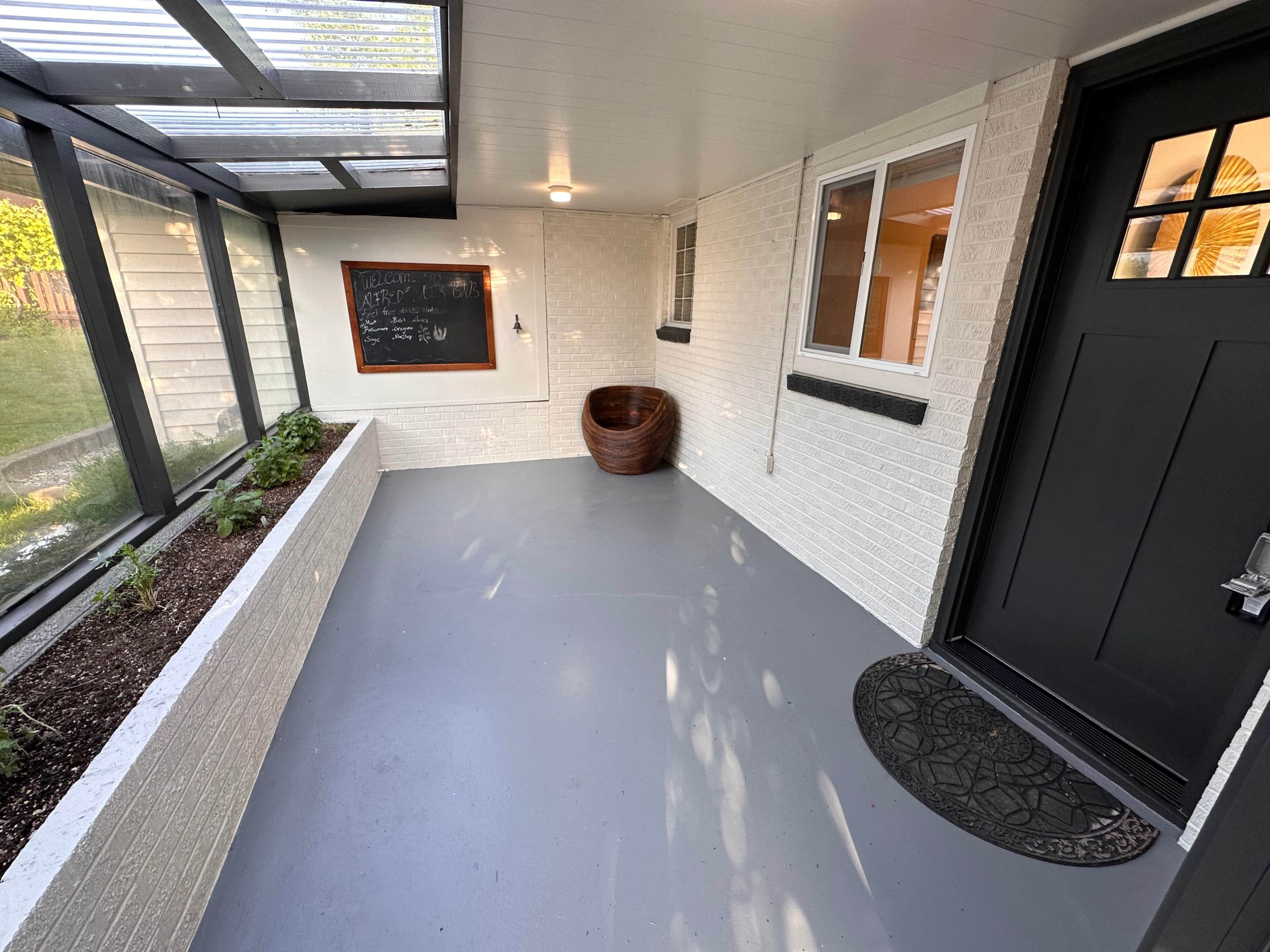 A covered outdoor area with a black door, a window, and a chalkboard with a welcome message.