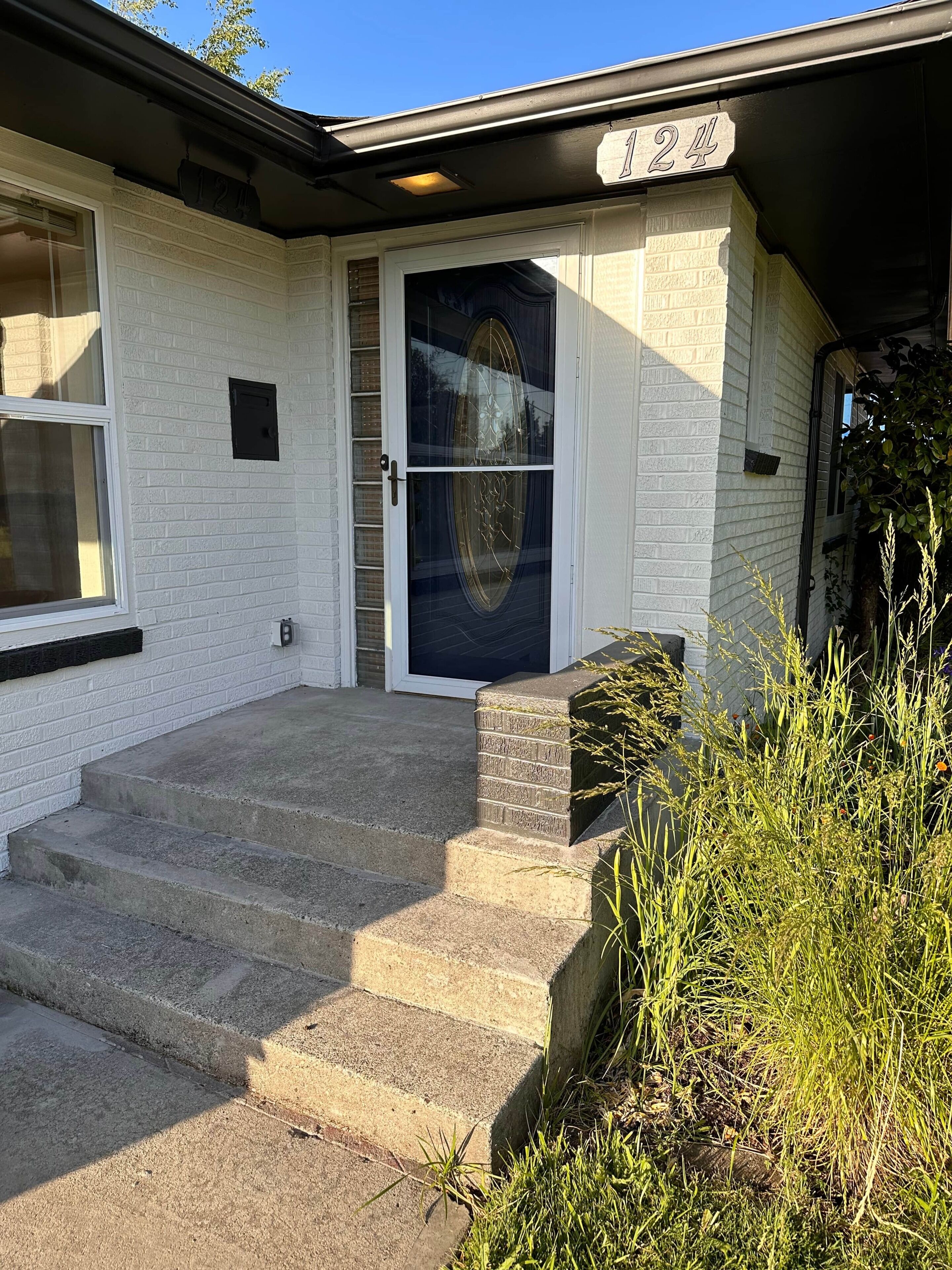 Ett hus med vit fasad, en svart ytterdörr och en trappa av betong som leder upp till entrén.