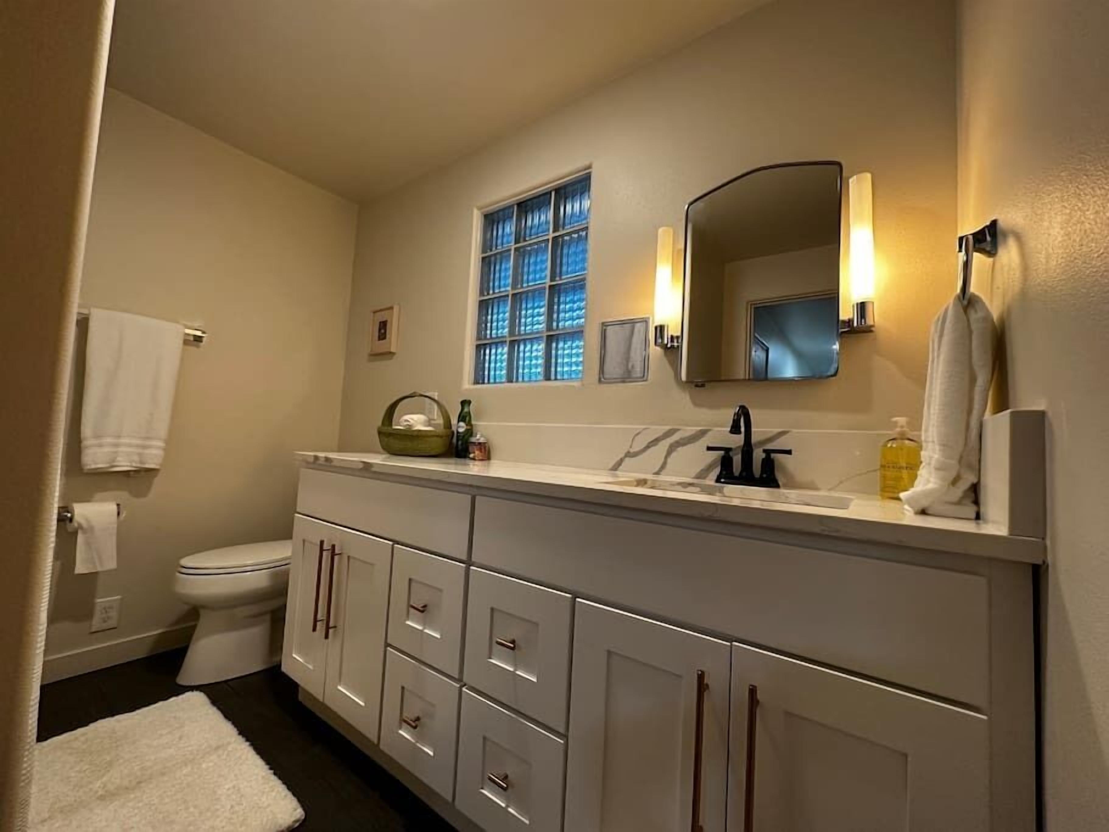 Ein Badezimmer mit Toilette, Waschbecken mit Spiegel und Fenster mit blau getöntem Glas.