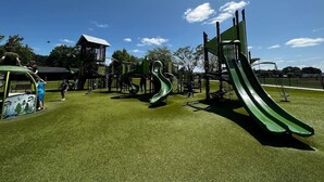 Ein Spielplatz mit mehreren Rutschen und Klettergerüsten, umgeben von einem Zaun und Bäumen.