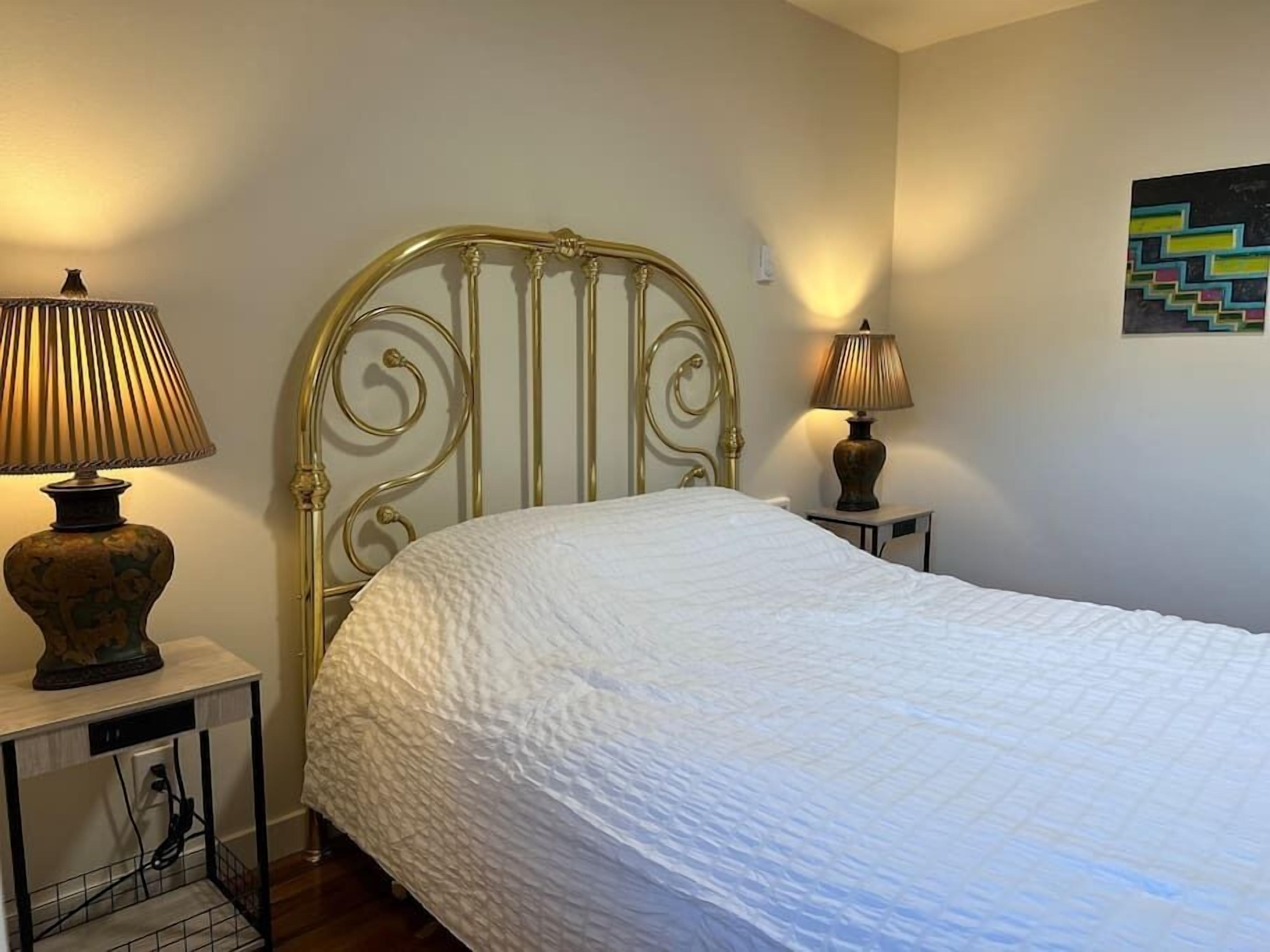 A neatly made bed with a white quilt, two bedside lamps, and a wall art piece.