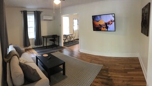 Ein Wohnzimmer mit einer Couch, einem Couchtisch, einem an der Wand befestigten Fernseher und Holzboden.