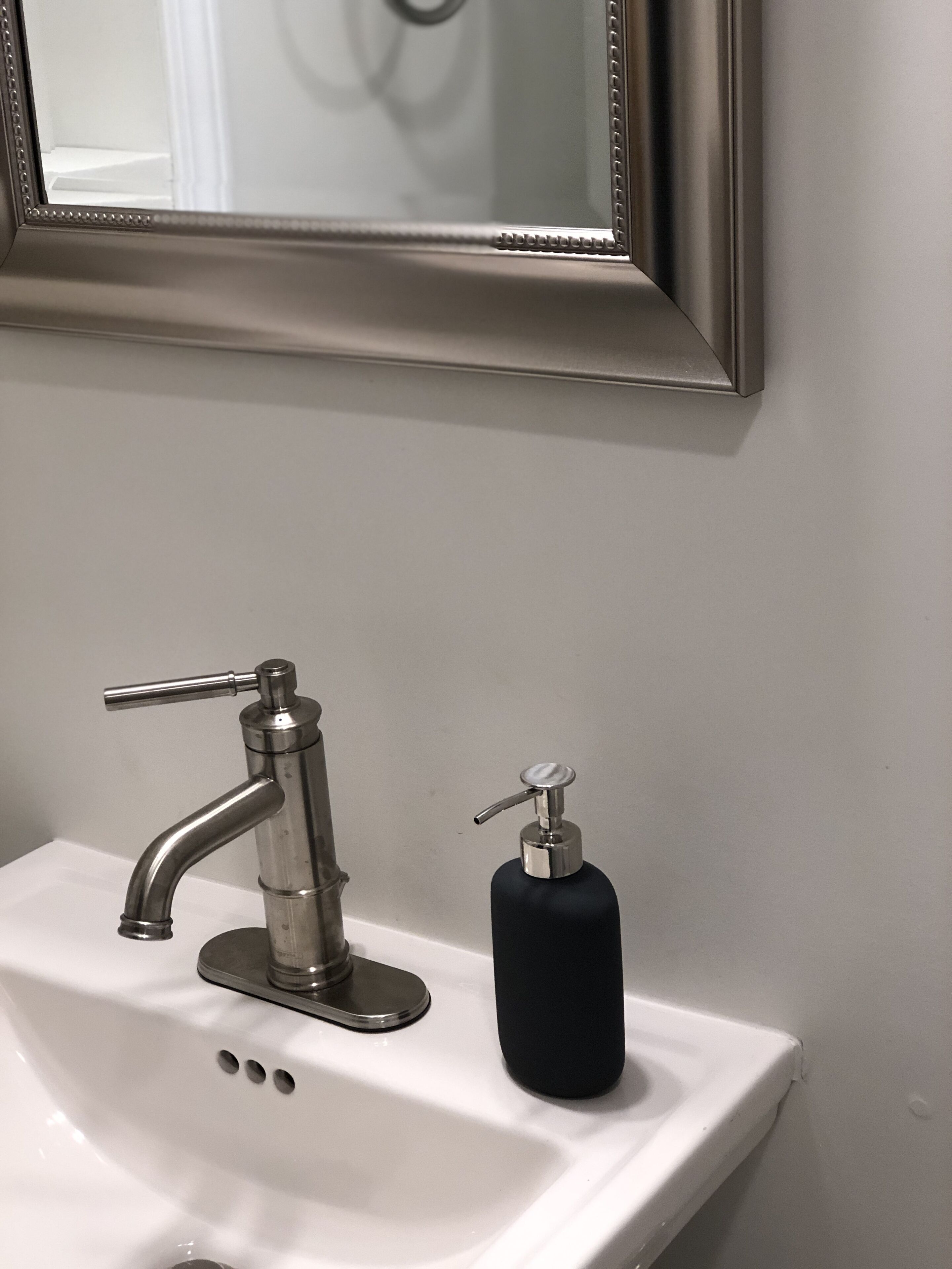 A bathroom sink with a modern faucet and a black soap dispenser.