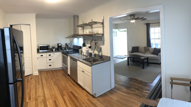 Eine moderne Küche mit weißen Schränken, einer Granit-Arbeitsplatte und Edelstahlgeräten. Ein Essbereich mit einer Couch und einem Couchtisch vorhanden.