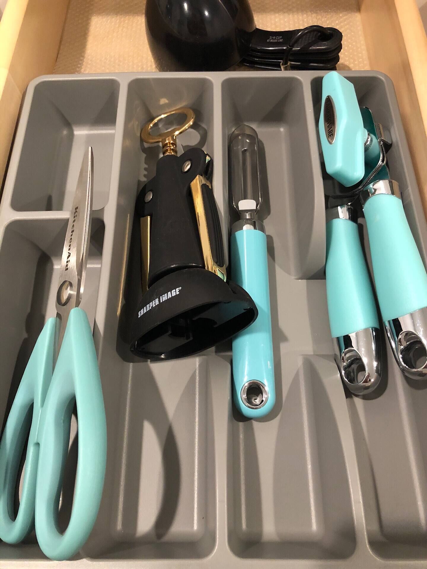 Un rangement gris, doté de compartiments, contenant une paire de ciseaux, un briquet noir et turquoise, et un autre briquet noir et turquoise muni d’un porte-clés.
