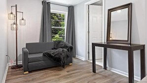 Ein modernes Wohnzimmer mit grauem Sofa, Holzboden, einer hohen Stehlampe, einem dunklen Holzkonsole und einem großen Spiegel.