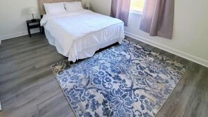 Een slaapkamer met een bed, nachtkastje, plafondventilator en een raam met gordijnen.