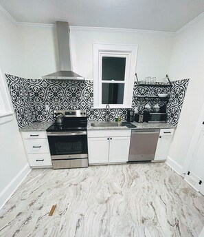 A kitchen with patterned backsplash, white cabinets, a stove, oven, and a dishwasher.