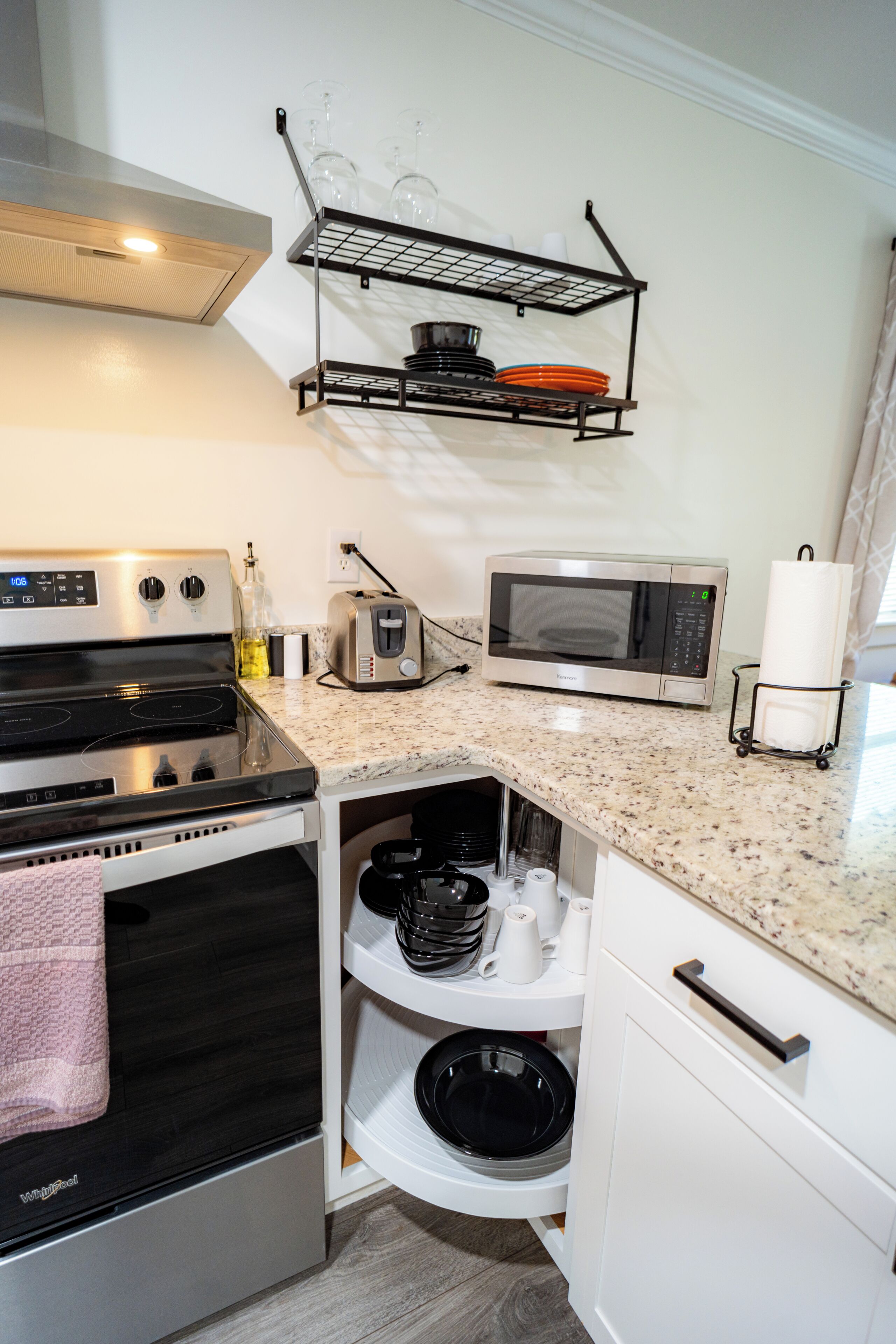 A compact kitchen with a stove, microwave, and a shelf above holding dishes and glasses.