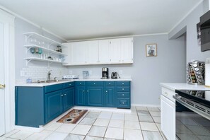 Une cuisine avec des meubles de rangement blancs, des meubles de rangement bleus en partie basse, une machine à café et un étagère à épices.