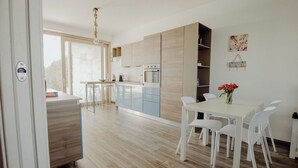Eine moderne Küche mit hellen Holzschränken, einer weißen Arbeitsplatte und einem Essbereich mit weißen Stühlen und einem Tisch.