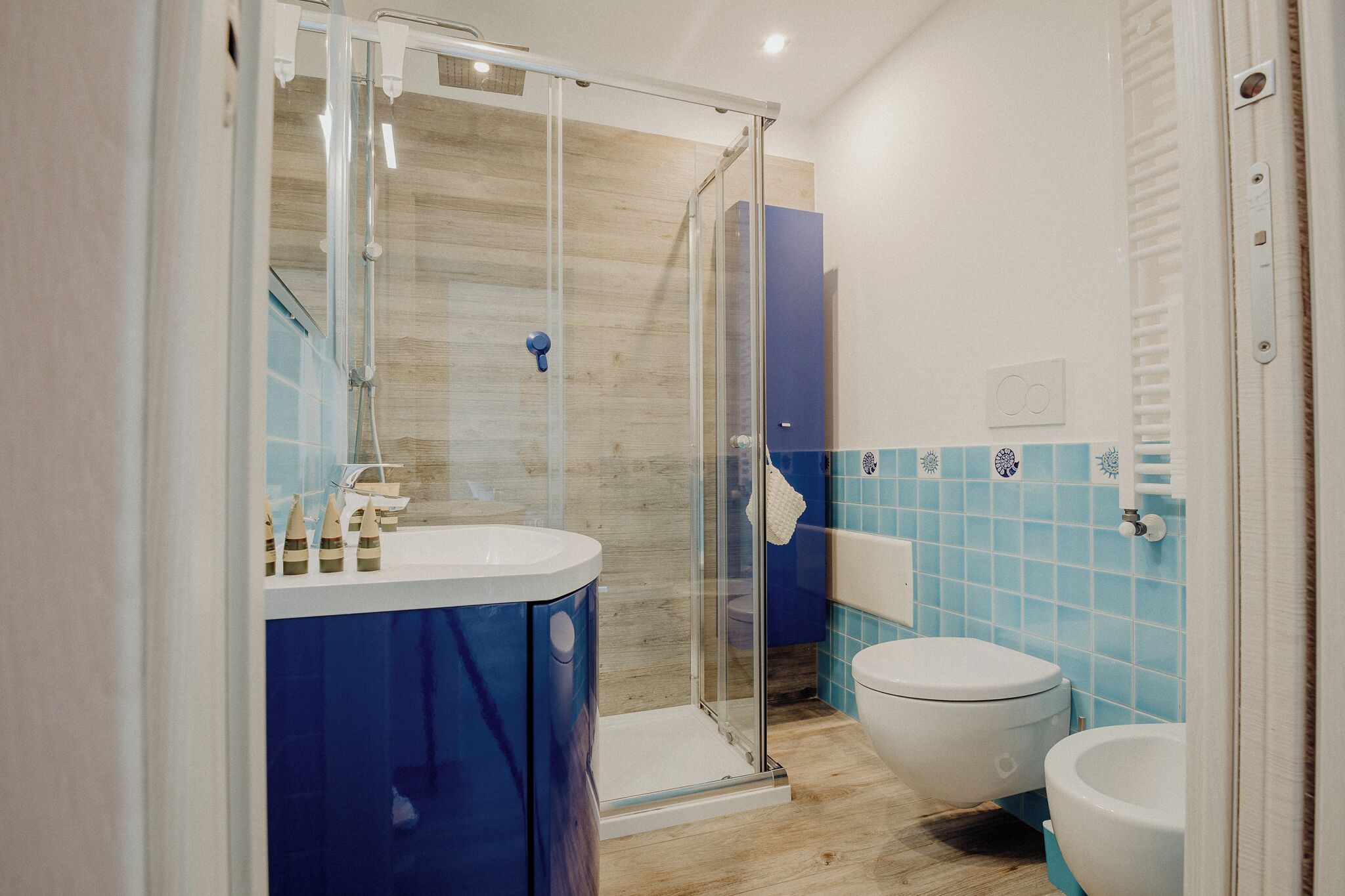 A modern bathroom with a glass shower enclosure, a white toilet, and a blue-tiled wall.
