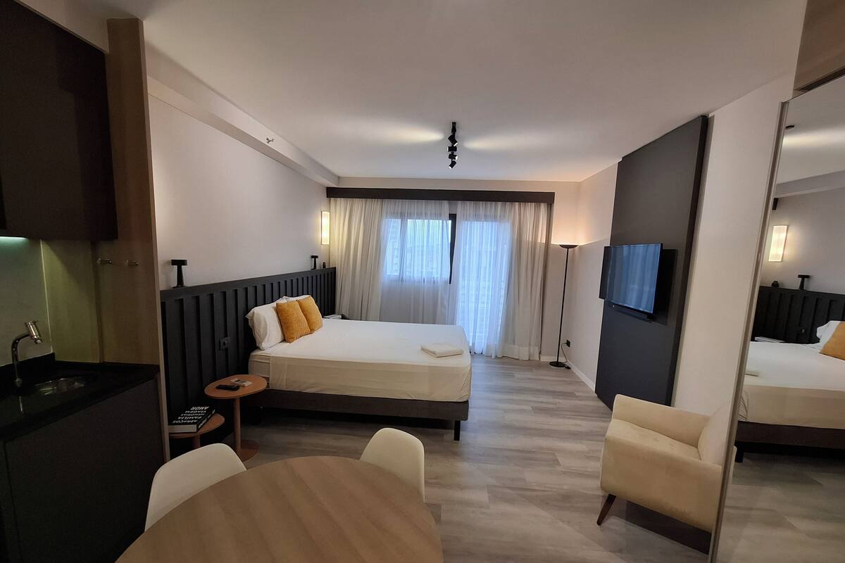 Une chambre d’hôtel comprenant un lit, une table de chevet, une lampe, une télévision et un coin repas avec des chaises et une table.