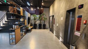 Un hall d’entrée moderne avec un escalier, des étagères à livres, des plantes en pot et un ascenseur.