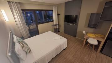 A hotel room with a bed, a TV, a desk with two chairs, and a window with curtains.