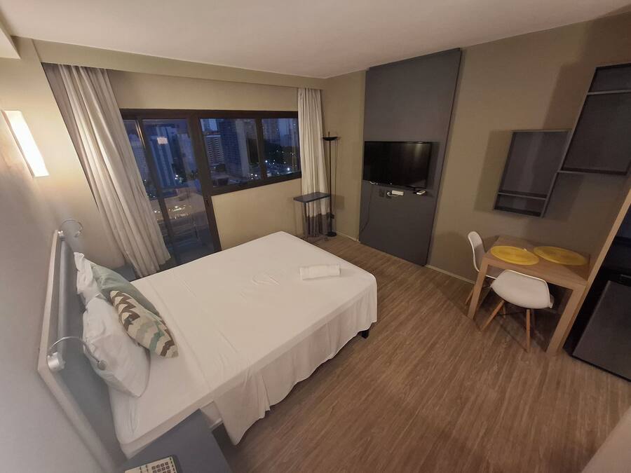 A hotel room with a bed, a TV, a desk with two chairs, and a window with curtains.