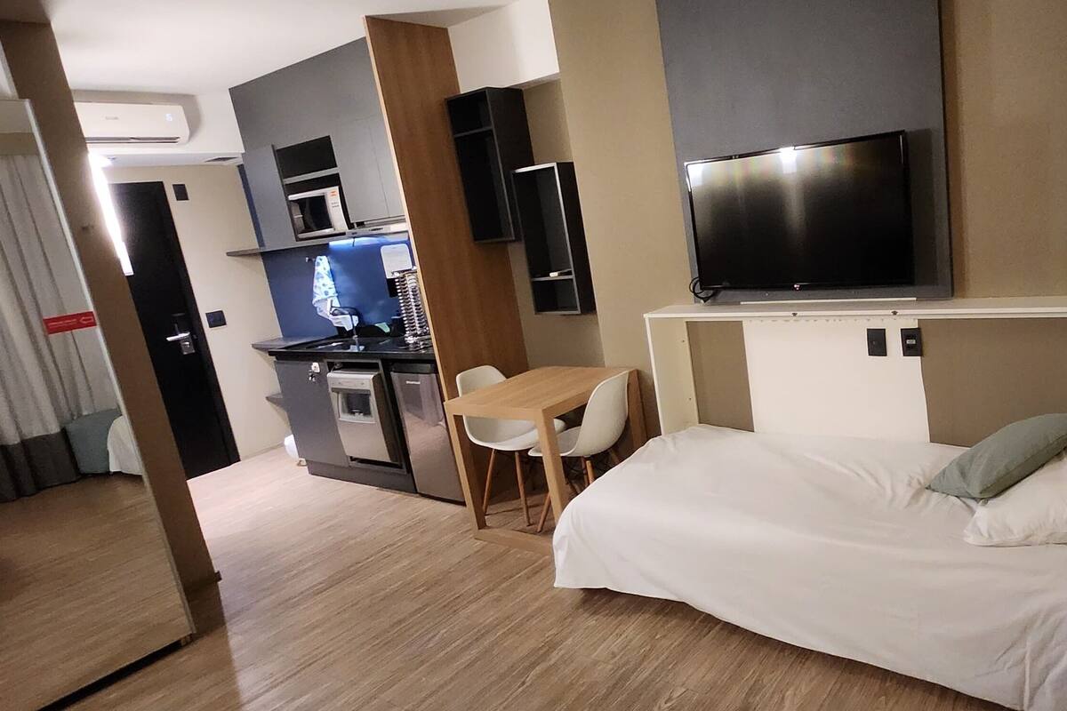 Une chambre d’hôtel de taille réduite, comprenant un lit, un bureau, une chaise, une télévision et une kitchenette.