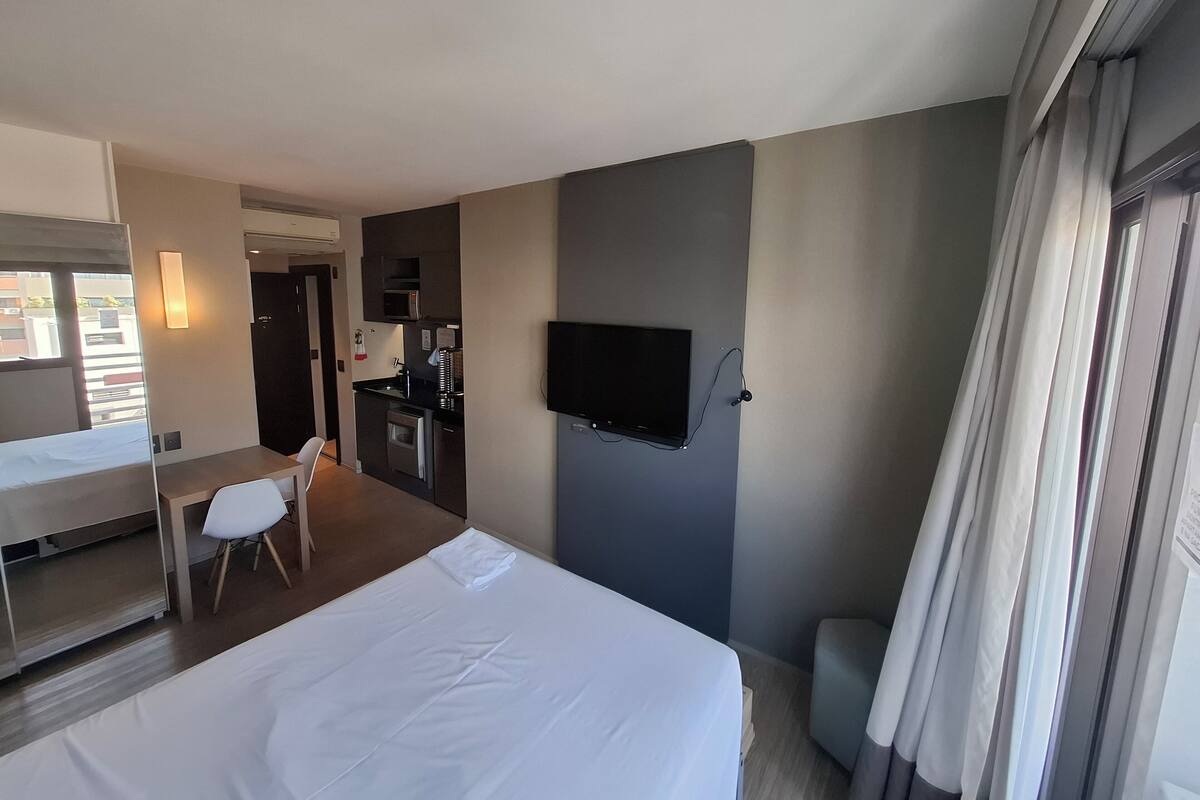 Une chambre d’hôtel équipée d’un lit, d’un bureau, d’une chaise, d’une télévision et d’une kitchenette.